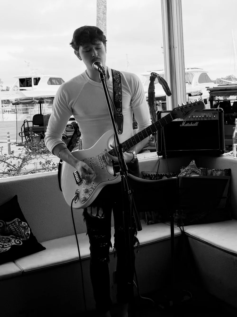 Jacob Muisi singing and playing electric guitar beside waterfront windows